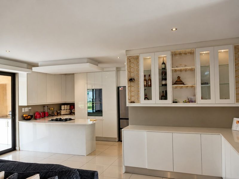 Modern kitchen featuring sleek white cabinetry, a central island with a gas hob, built-in oven, and elegant glass-fronted display units with integrated lighting.