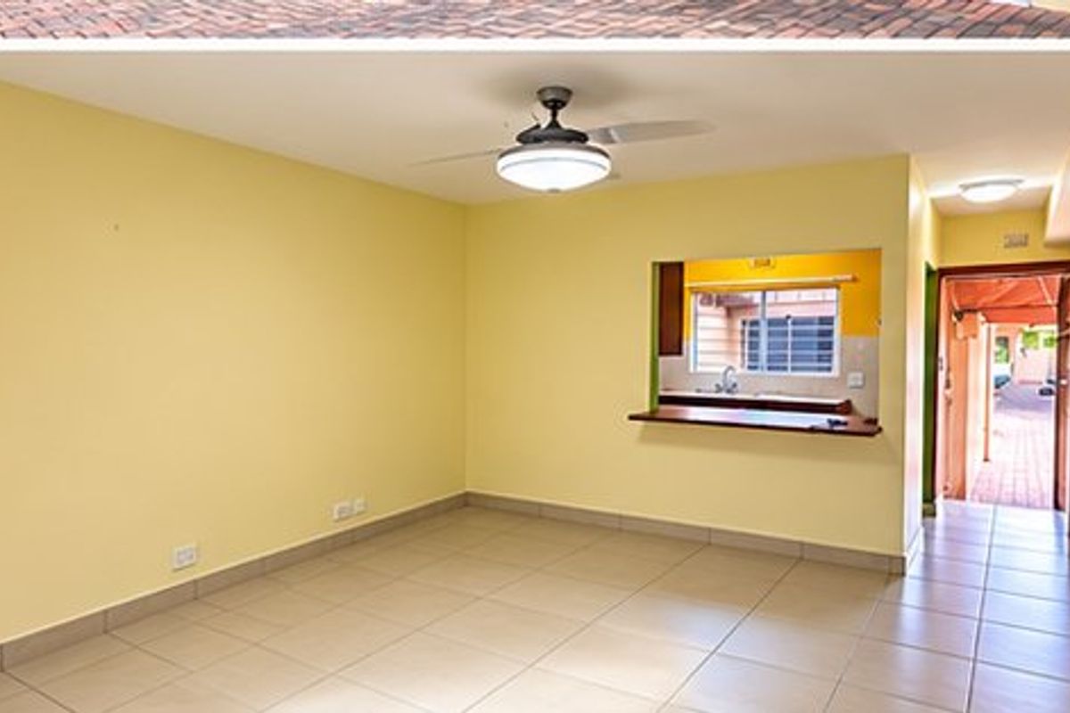 An empty living room featuring tiled flooring, a ceiling fan, and a convenient pass-through window connecting to the kitchen area.
