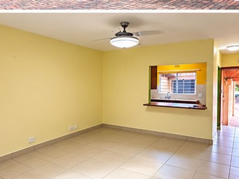 An empty living room featuring tiled flooring, a ceiling fan, and a convenient pass-through window connecting to the kitchen area.
