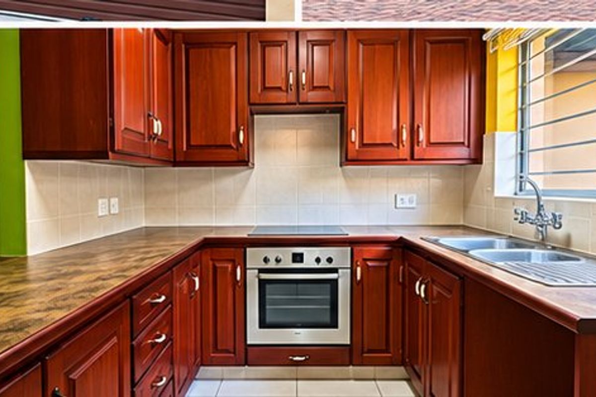 A functional kitchen featuring wooden cabinetry, laminate countertops, a built-in oven and hob, and a double sink with a window view.