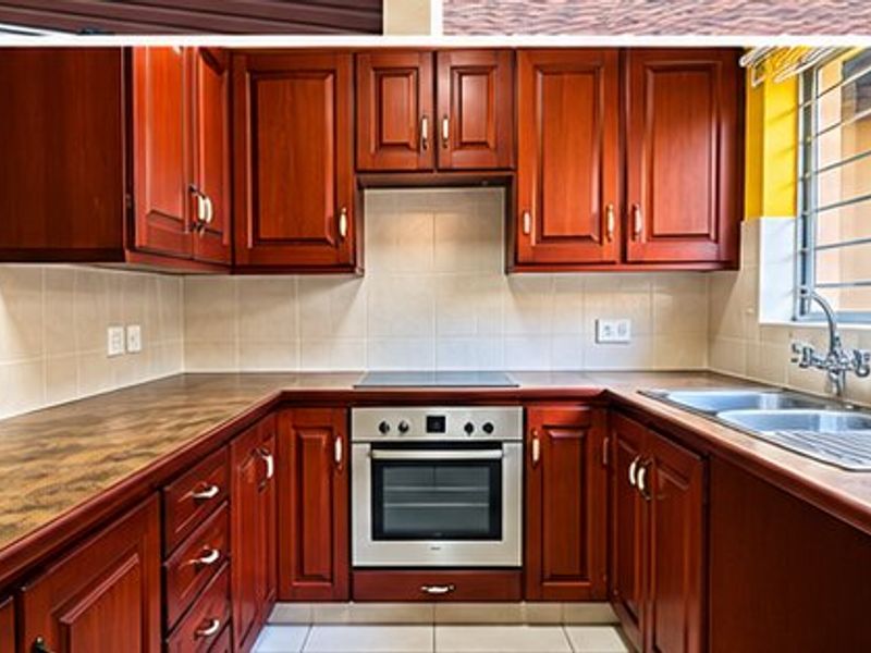 A functional kitchen featuring wooden cabinetry, laminate countertops, a built-in oven and hob, and a double sink with a window view.