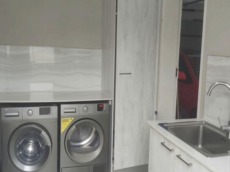 A clean and functional laundry area featuring modern built-in cabinetry, a stainless steel sink with mixer tap, and a stone-look splashback.