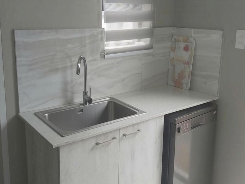A compact scullery area featuring a stainless steel sink, stone countertop, and marble-look splashback with integrated cabinetry.
