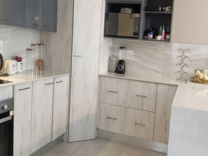 Modern kitchen featuring light wood-grain cabinetry, stone countertops, marble-effect splashbacks, and integrated stainless steel oven and hob.