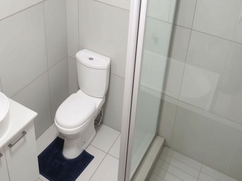 A modern, well-maintained bathroom featuring a vessel sink vanity, a standard toilet, and a glass-enclosed shower with neutral wall and floor tiling.