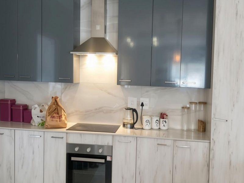 Modern kitchen featuring high-gloss grey upper cabinets, marble-effect lower cabinetry, stone countertops, and integrated stainless steel appliances.