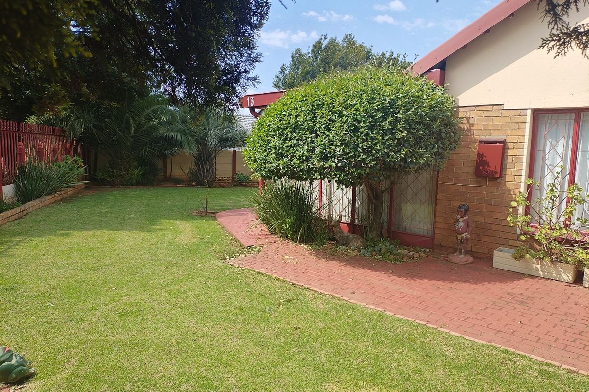 A well-maintained rear garden featuring a brick-paved pathway, established lawn, and secure perimeter fencing.