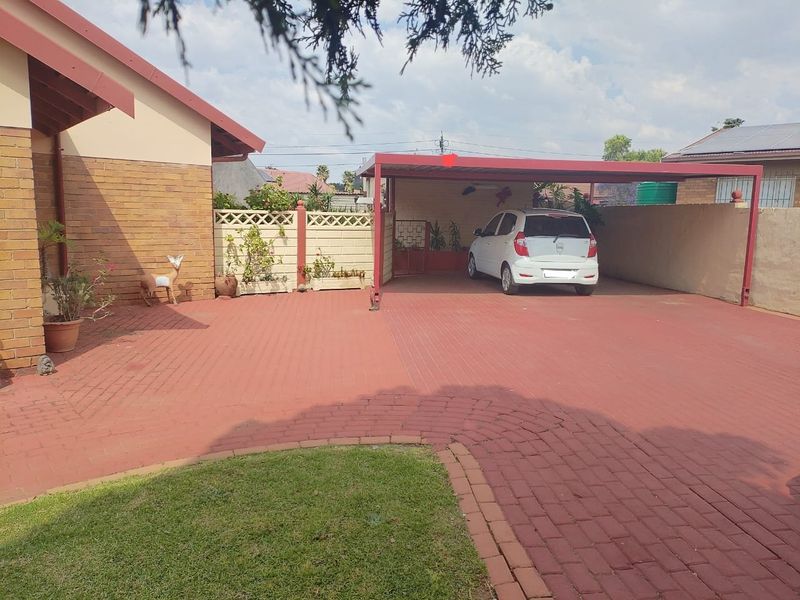 Front exterior view featuring a paved driveway, a covered carport, and brick boundary walling.
