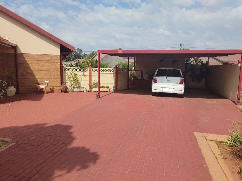 Front exterior view featuring a paved driveway and a covered carport structure with brick boundary walling.