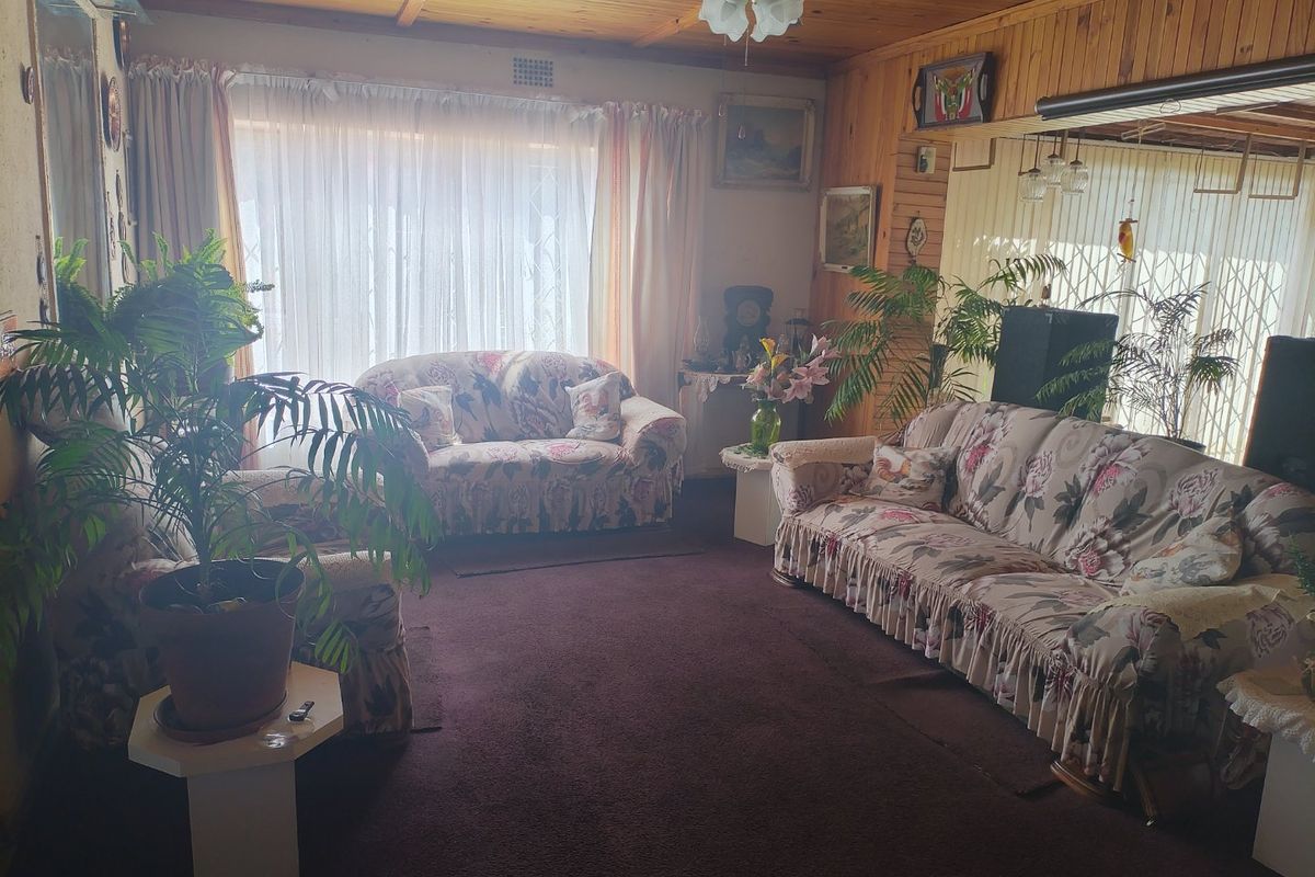 A living room featuring timber-clad walls and ceiling, a central ceiling fan, and carpeted flooring, offering a dated aesthetic ready for modernization.