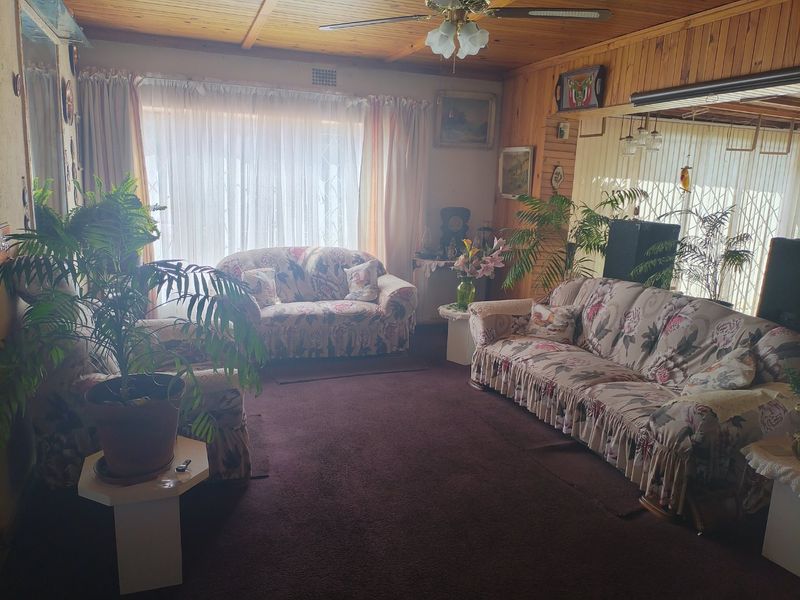 A living room featuring timber-clad walls and ceiling, a central ceiling fan, and carpeted flooring, offering a dated aesthetic ready for modernization.