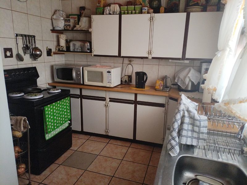 A functional kitchen featuring dated cabinetry, laminate countertops, ceramic tiling, and a freestanding stove, offering potential for a modern renovation.