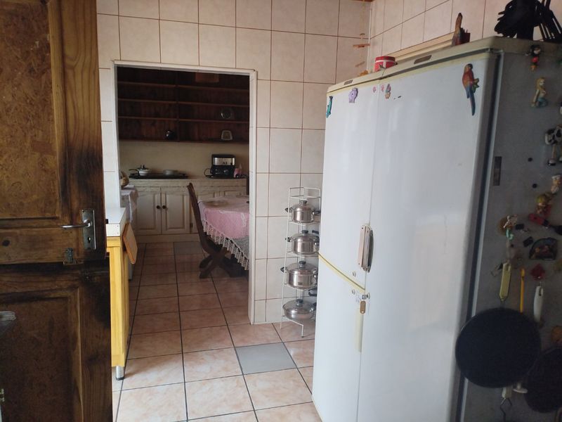 A dated kitchen area featuring tiled flooring and walls, with a view into an adjacent dining space with wooden cabinetry.