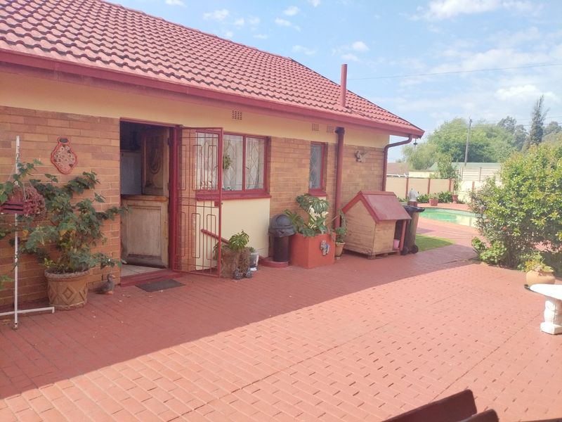 Rear exterior view of the house featuring brick paving, a tiled roof, and access to a swimming pool area.