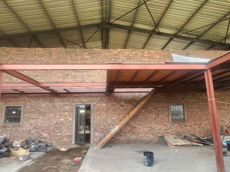 Industrial utility space featuring exposed brick walls, steel beam framework, and an unfinished mezzanine level with a timber staircase.