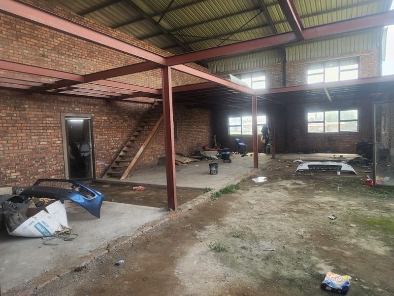 Spacious industrial utility area featuring exposed brick walls, steel structural beams, a mezzanine level with staircase, and concrete flooring.