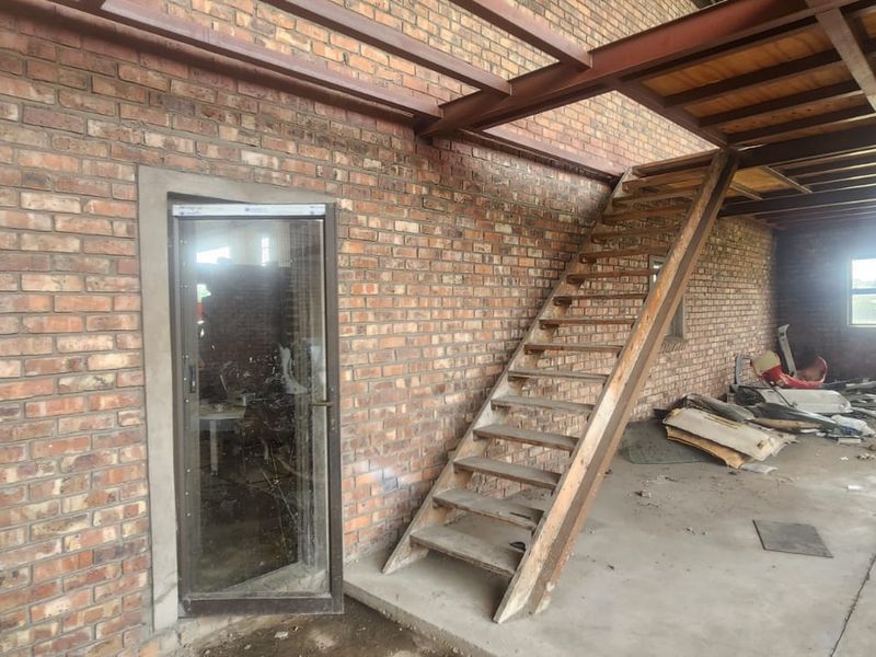 Industrial utility space featuring exposed brick walls, concrete flooring, and a timber staircase leading to an upper level, suitable for workshop or storage use.