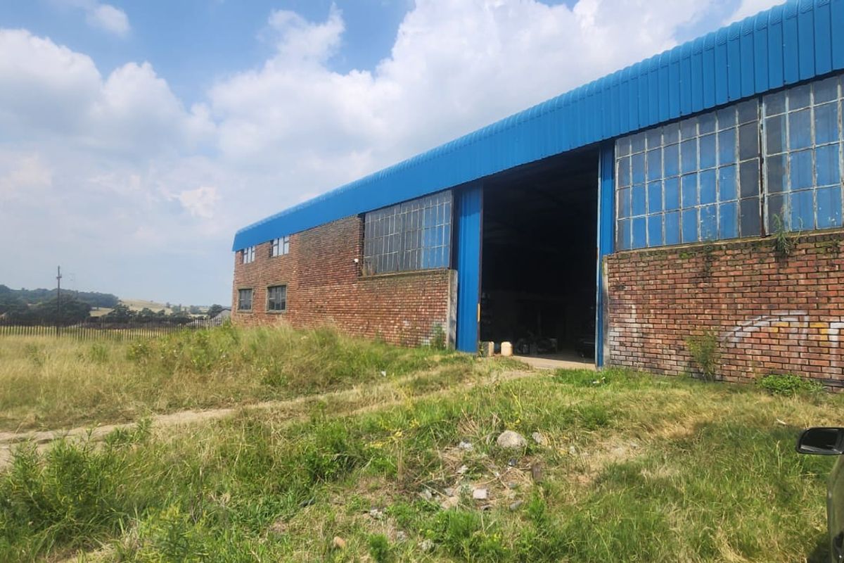 Industrial warehouse building featuring a brick facade, large sliding access door, and steel-framed windows, set on a large open plot.