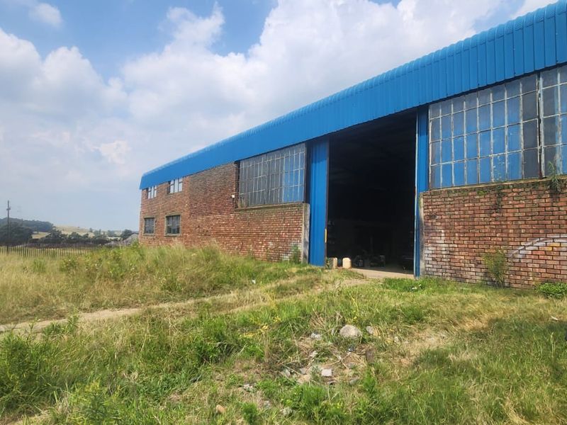 Industrial warehouse building featuring a brick facade, large sliding access door, and steel-framed windows, set on a large open plot.