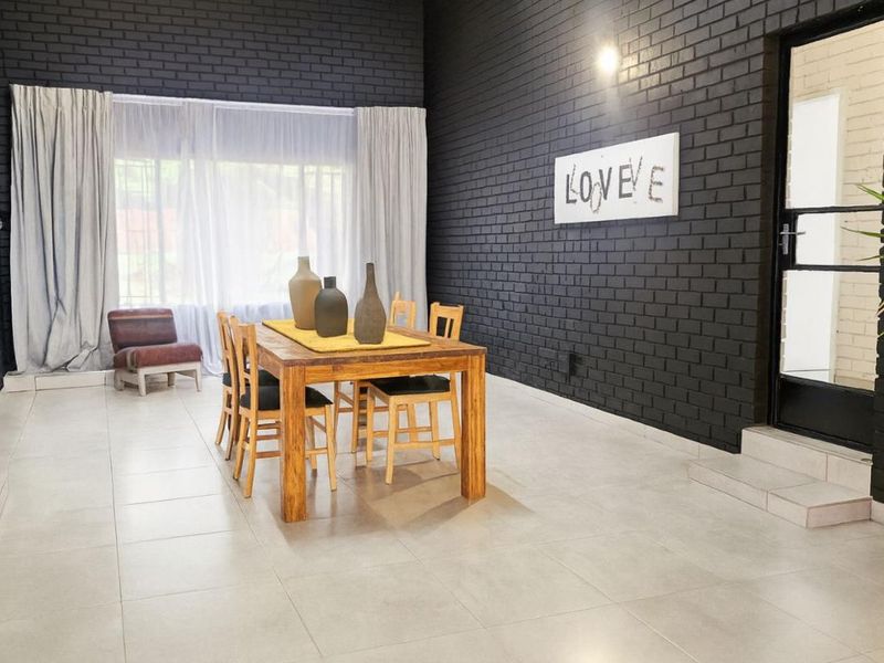 Spacious dining area featuring modern dark painted brick walls, large windows with natural light, and neutral tiled flooring.