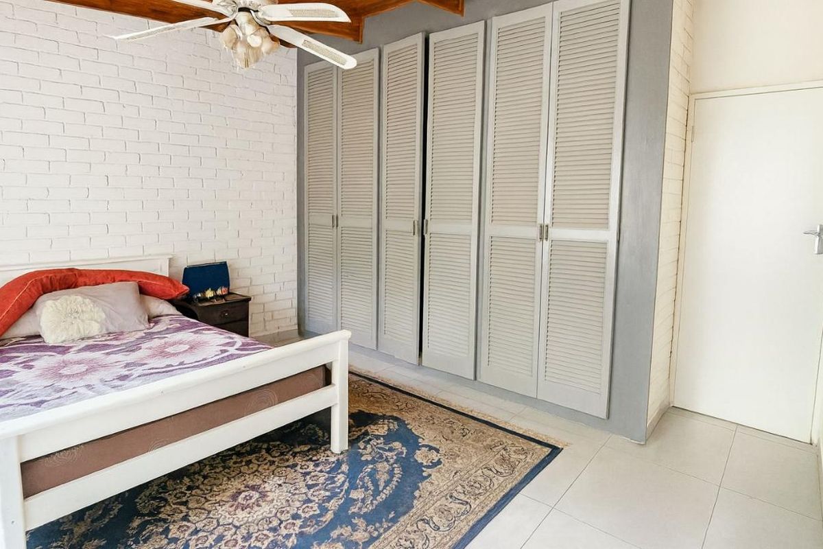 Bedroom featuring built-in louvered cupboards, exposed white brick wall, tiled flooring, and a ceiling fan.