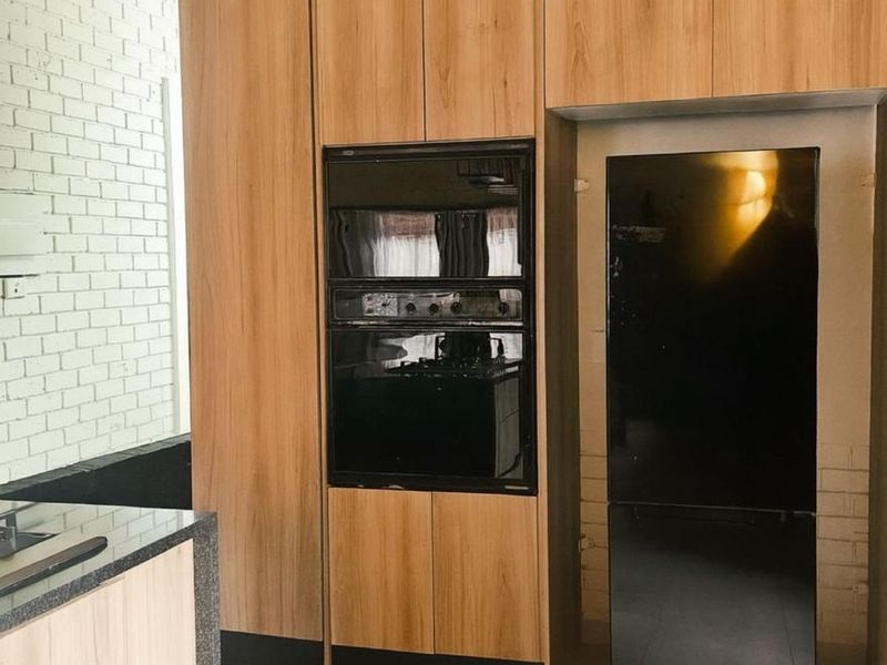 Modern kitchen featuring wood-look cabinetry, built-in oven, exposed timber ceiling beams, and a painted brick wall with tiled flooring.