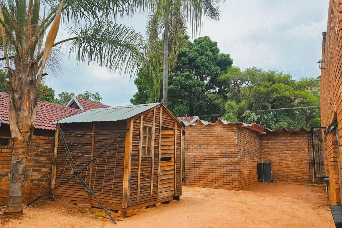 Rear exterior area featuring a brick boundary wall and a wooden storage shed set on an exposed earth yard.