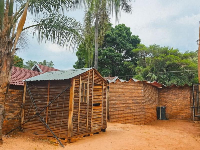 Rear exterior area featuring a brick boundary wall and a wooden storage shed set on an exposed earth yard.
