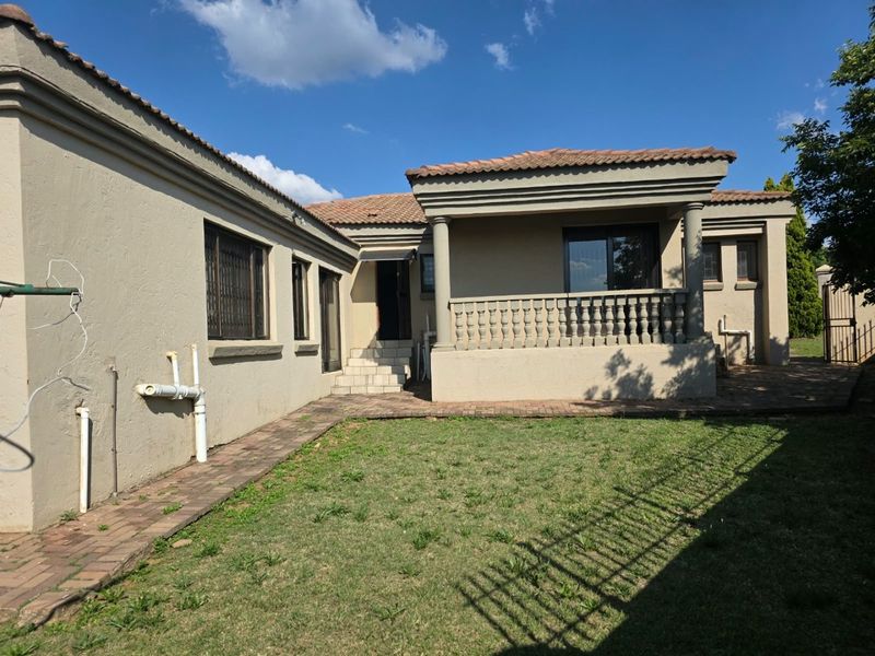 Rear view of the property featuring a covered patio with concrete columns, balustrade, paved walkway, and a small garden area.