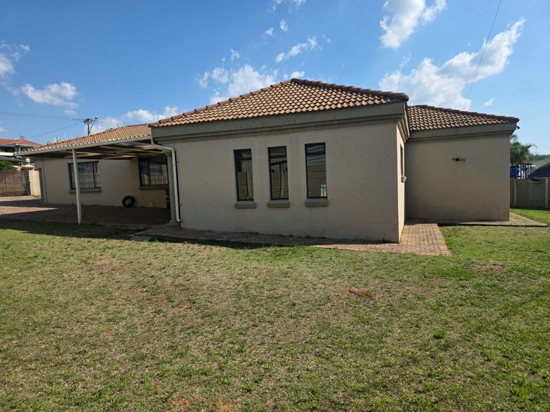 Rear view of the house featuring a tiled roof, a covered patio area, and a paved walkway leading across the garden.