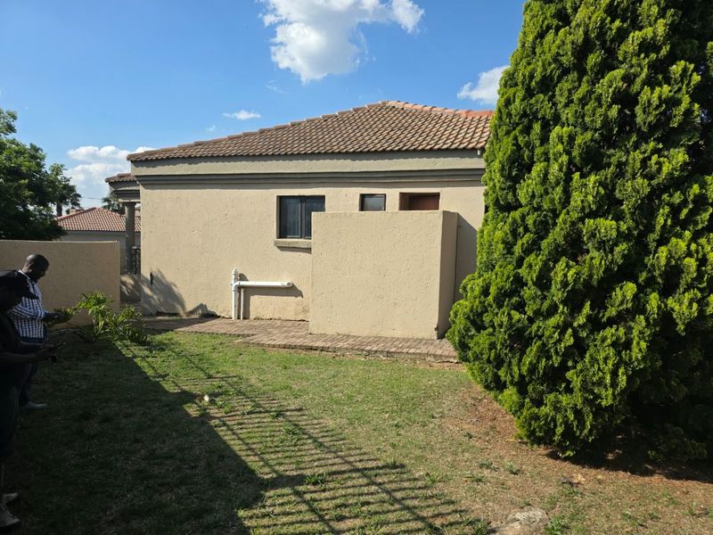 Rear view of the property showing a tiled roof, paved area, and exterior wall with visible plumbing fixtures.
