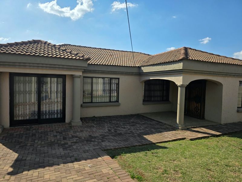 Rear view of the house featuring a paved patio area, tiled roof, and secure sliding door access to the interior.