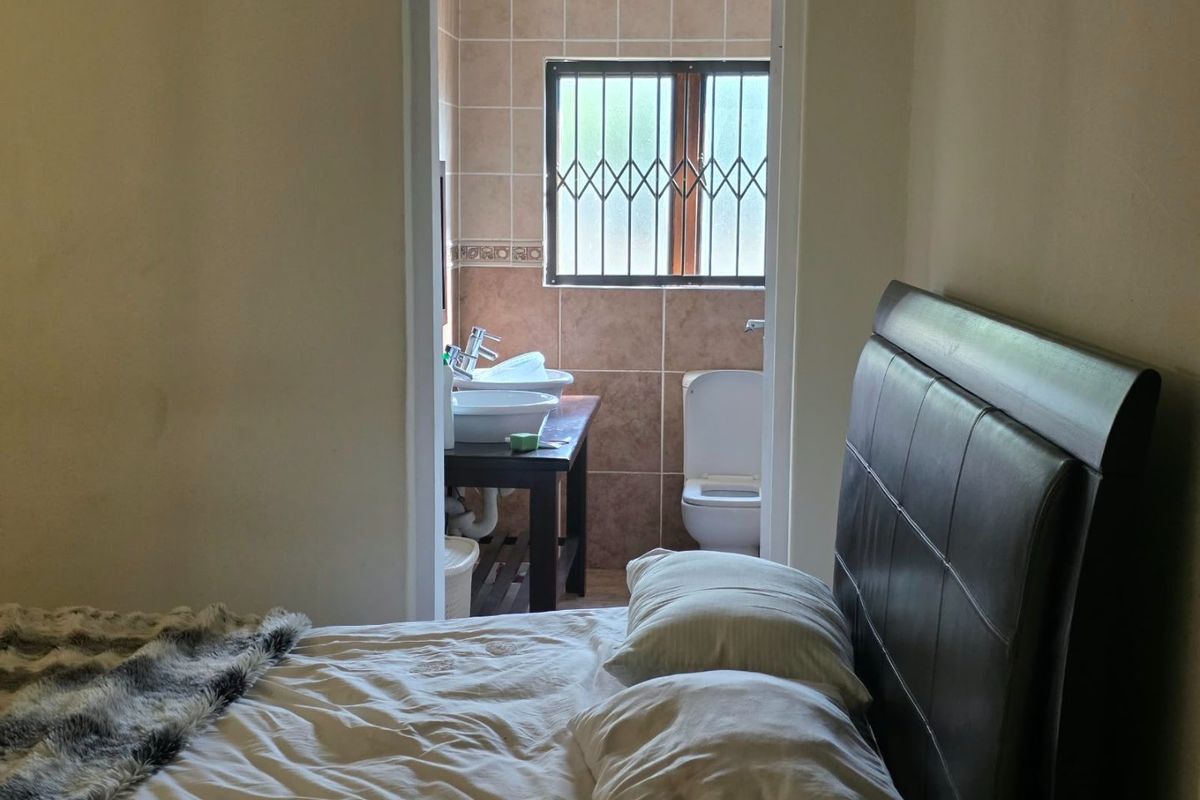 Bedroom with an en-suite bathroom featuring tiled walls, a vanity, and a window with security bars.