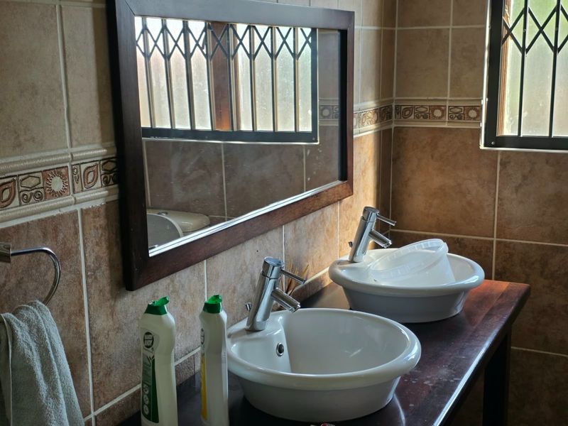 A bathroom featuring a double vanity with ceramic vessel sinks, chrome mixer taps, and decorative tiled walls.
