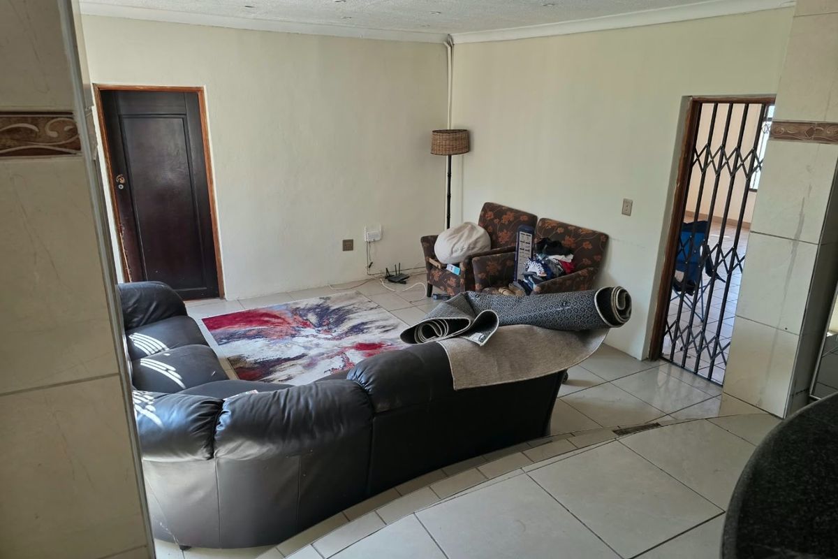 A living room area featuring tiled flooring, recessed lighting, and a security gate, presenting a dated interior in need of cosmetic updates.