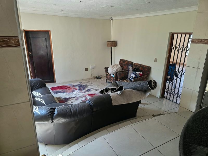 A living room area featuring tiled flooring, recessed lighting, and a security gate, presenting a dated interior in need of cosmetic updates.
