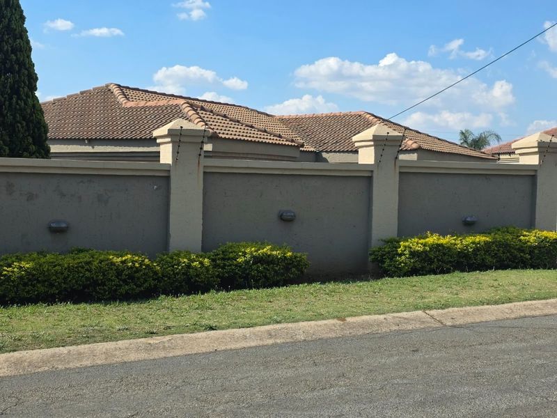 Street view of the property featuring a perimeter wall with electric fencing, tiled roof, and exterior wall lighting.