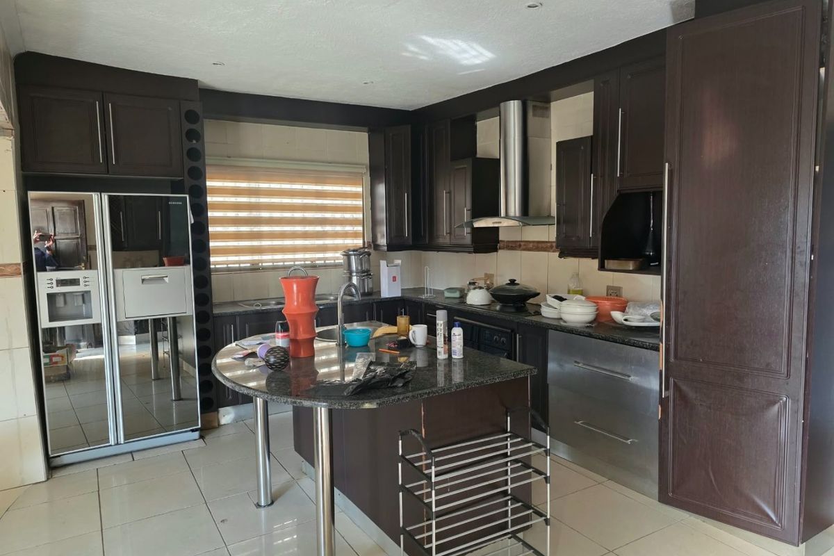 Spacious kitchen featuring dark wood cabinetry, granite countertops, stainless steel extractor fan, and tiled flooring with a central island prep area.
