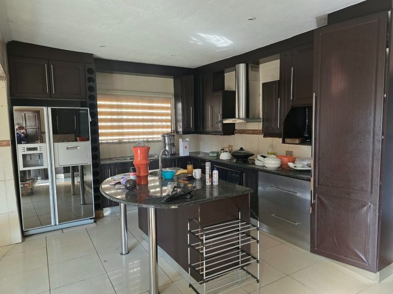 Spacious kitchen featuring dark wood cabinetry, granite countertops, stainless steel extractor fan, and tiled flooring with a central island prep area.