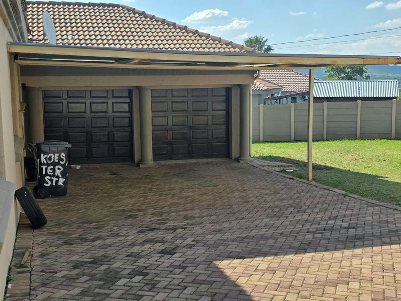 A double garage with a paved driveway and an attached carport, featuring a tiled roof and precast concrete boundary walling.