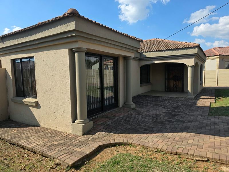 Rear exterior view of the house featuring a paved patio area, decorative columns, and sliding glass doors leading into the living space.