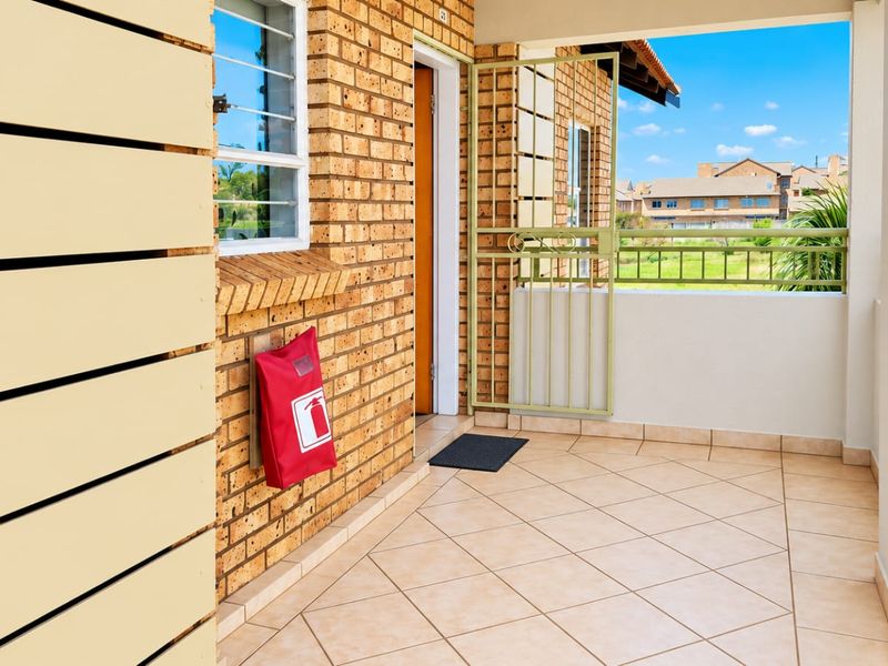A clean, covered balcony featuring brick wall finishes, tiled flooring, and a secure metal gate, offering a pleasant outdoor space.