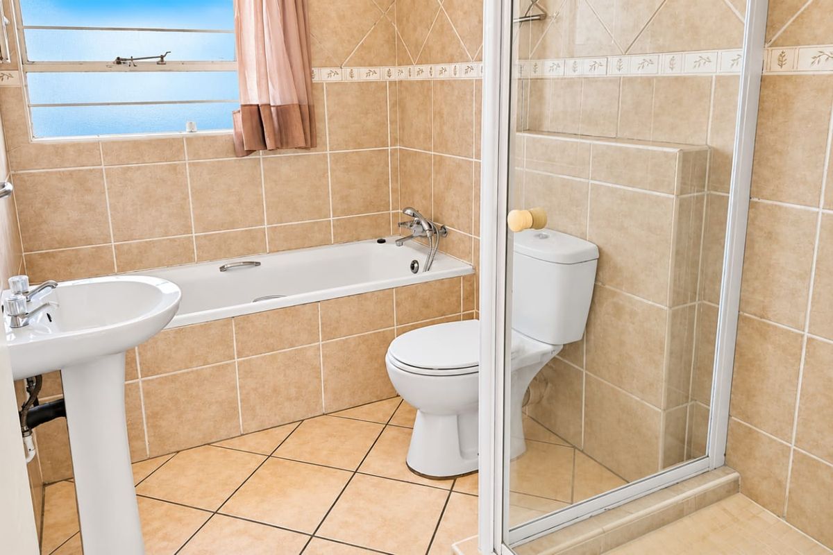 A functional bathroom featuring a pedestal basin, built-in bathtub, toilet, and a separate shower enclosure with neutral ceramic tiling throughout.