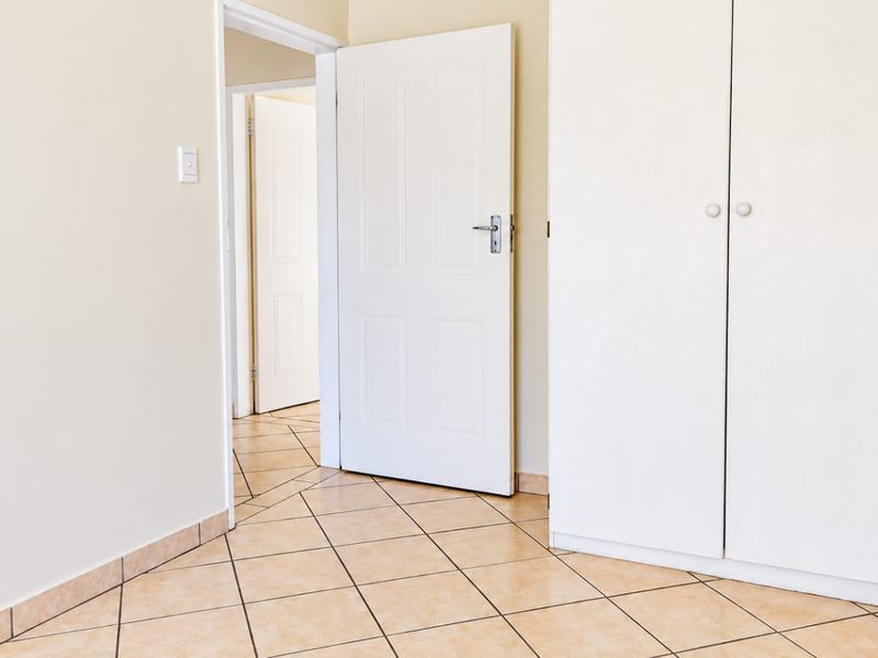 A clean, empty bedroom featuring neutral tiled flooring and built-in cupboards, offering a versatile space ready for personalization.
