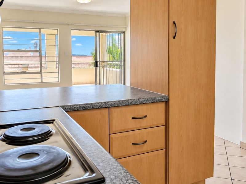 A functional kitchen featuring built-in cabinetry, laminate countertops, and an electric hob, with direct access to an outdoor balcony area.