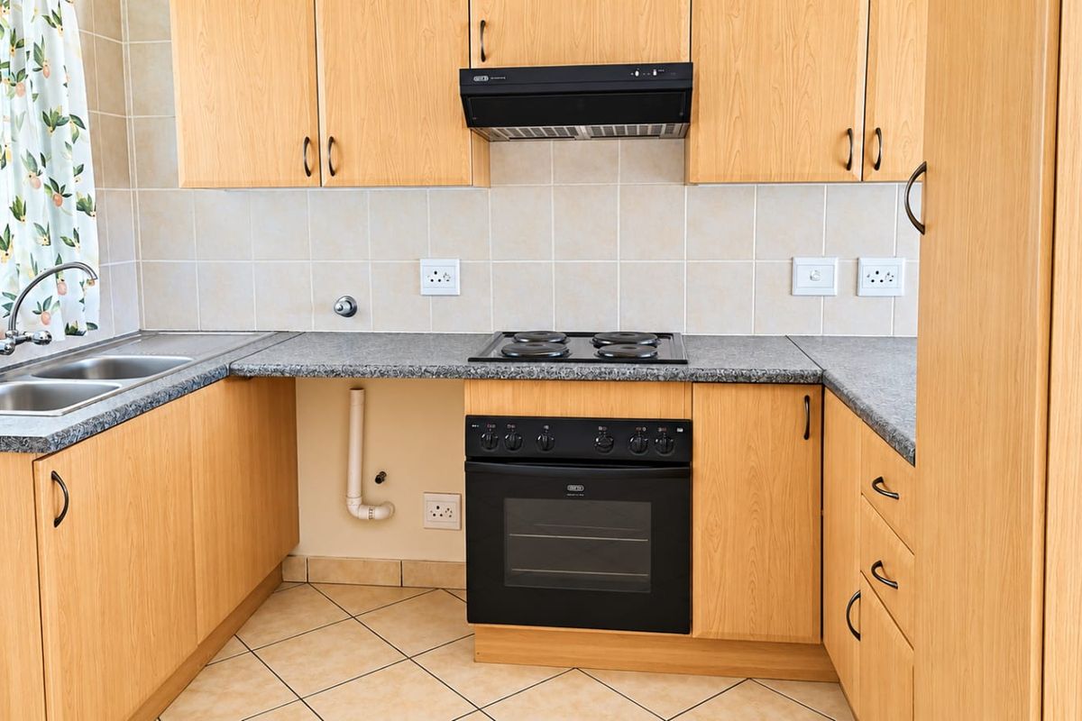 A functional kitchen featuring light wood-look cabinetry, granite-style countertops, a built-in oven with hob, and a double stainless steel sink with tiled backsplash.