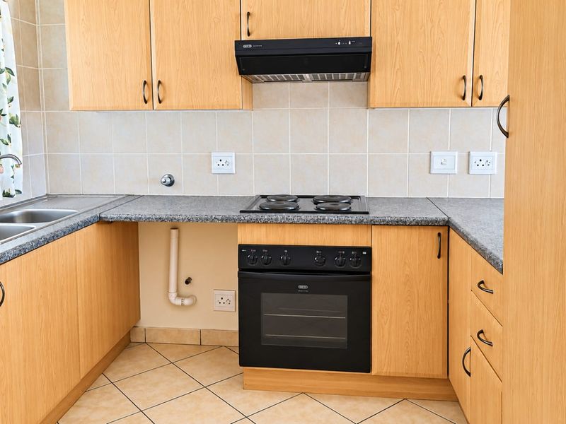 A functional kitchen featuring light wood-look cabinetry, granite-style countertops, a built-in oven with hob, and a double stainless steel sink with tiled backsplash.