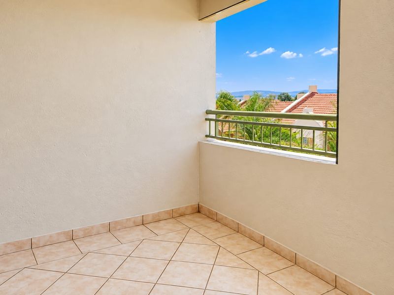 A clean, empty balcony featuring tiled flooring and a metal balustrade, offering an open view of the surrounding neighborhood.