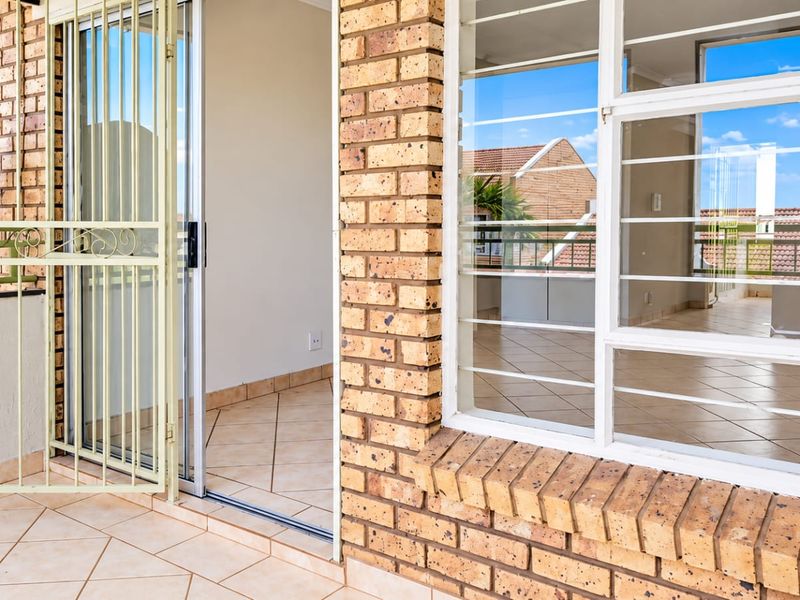 A tiled balcony area featuring exposed brickwork, a sliding glass door, and security gates, offering a clean and functional outdoor space.
