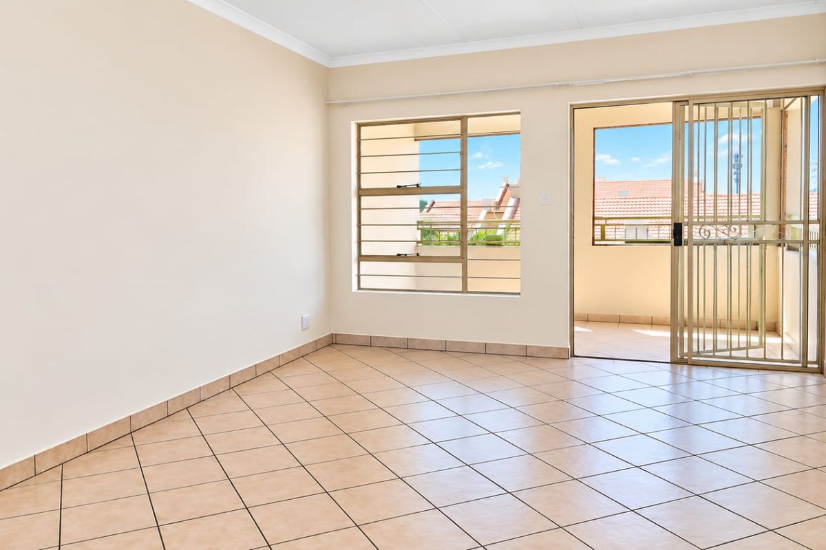 A bright, empty living room featuring tiled floors, a sliding glass door with a security gate, and access to an outdoor balcony area.